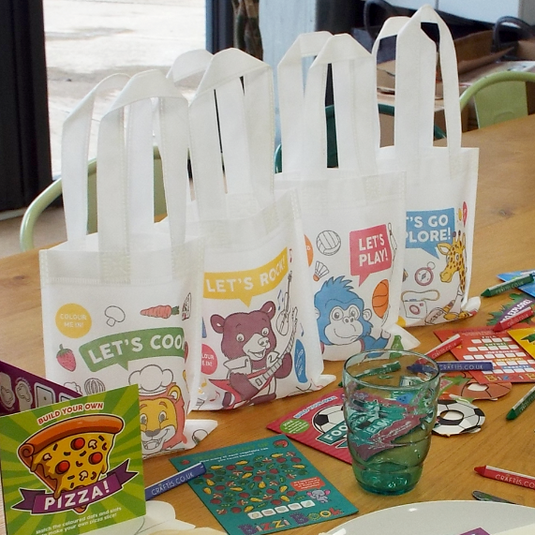 children's activity bags and crayons set up on a table with crayons, plates and glasses. 4 designs: Let's Cook, Let's Rock, Let's Play, Let's Go Explore